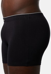 Boxer briefs neri in cotone con una vestibilità aderente. Presentano un elastico bianco in vita e una texture liscia. Vista laterale che mostra la forma e il taglio.