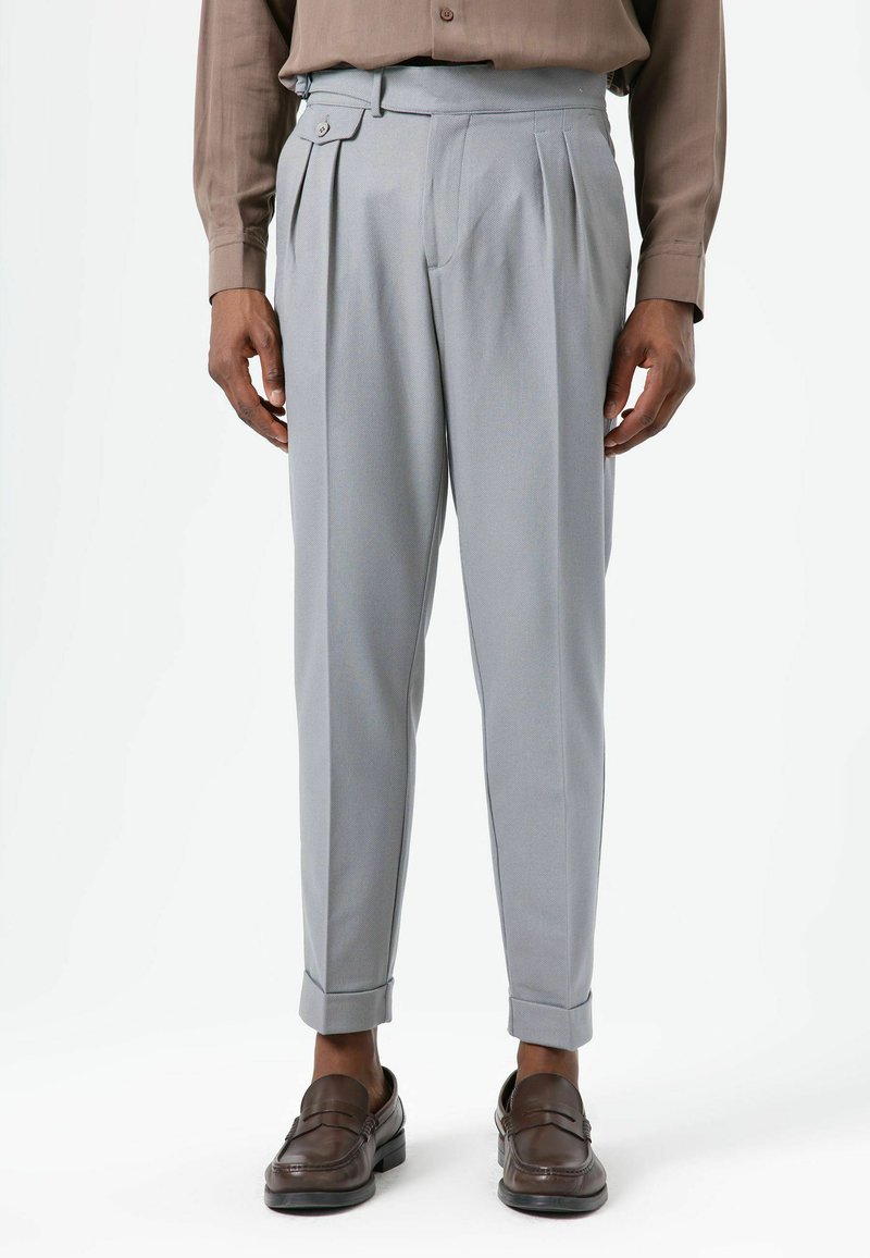 Pantalon gris clair ajusté avec plis, poches latérales et fermeture à bouton. Le tissu a une texture lisse, des revers roulés et une coupe droite.