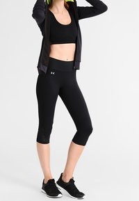 Leggings de sport noirs crop et un hoodie noir cropped avec des accents verts. Texture lisse, design ajusté et détails de logo sur la jambe et la manche.