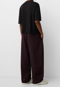 Svart kortärmad t-shirt med en lös passform, tillsammans med mörkröda vida byxor och ljusa sneakers. Minimalistisk design.