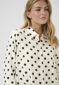 Camicia button-up in tessuto crema, con pois neri irregolari. Colletto classico e maniche lunghe con una vestibilità rilassata.