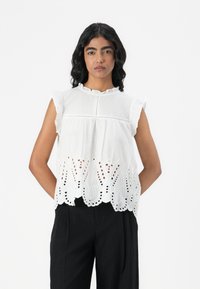 Blouse blanche sans manches avec un col froncé et une broderie en œillets complexe dans le bas, dotée d'une coupe décontractée et d'un tissu léger.