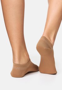 Calzini alla caviglia color sabbia con polsino a coste e motivo a zigzag, texture liscia e vestibilità aderente, progettati per restare fermi in posizione.