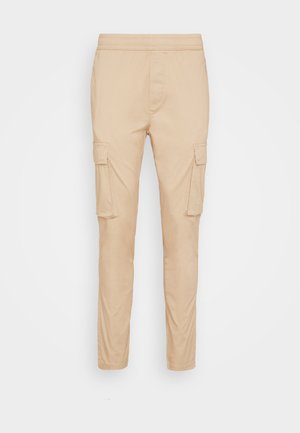 Pantalones cargo beige con una cintura elástica, dos bolsillos laterales y dos bolsillos en los muslos, fabricados con una tela suave y ligera.