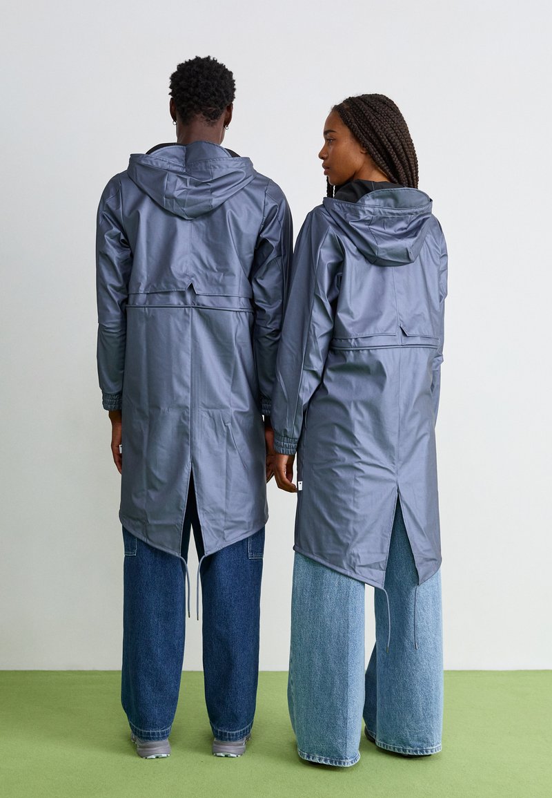 Grijze waterdichte jassen met capuchons, rugplooien en trekkoorden, gecombineerd met wijde spijkerbroeken in een gespleten wassing.