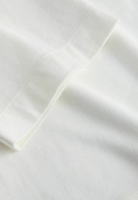 Valge puuvillane kangas, millel on sile tekstuur. Äärte servas nähtav õmblus lisab puhta ja lihtsa disaini.