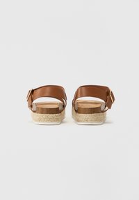 Sandali in pelle marrone con fibbia, suole in juta stile espadrille, tacco piatto, texture liscia e design semplice.
