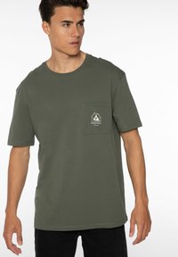 Olijfgroene katoen T-shirt met een ronde hals, korte mouwen en een linkerkant borstzak met een wit berglogo.