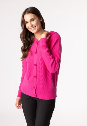 Fuchsiový cardigan s pleteným vzorem, zapínání na knoflíky a kapucí. Pletací textura; dlouhé rukávy a žebrované manžety; v kombinaci s černými kalhotami.