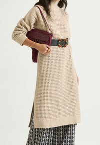 Vestito maglione beige lavorato a maglia con finitura testurizzata, abbinato a una cintura nera con decorazioni colorate e una borsa a tracolla bordeaux.