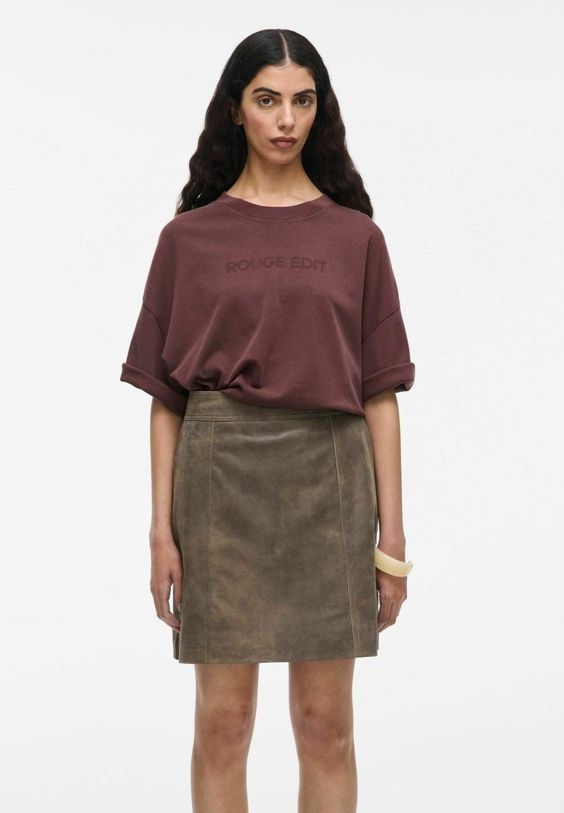 Bordo arba oversized marškiniai su užrašu "ROUGE EDIT", derinami su rudos zomšinės mini sijonu. Modelis dėvi skaidrų apyrankę ant vienos rankos.