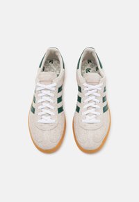 Beige mockasneakers med gröna ränder, vita skosnören och en sula av gummiblandning. Insidan har en mönstrad innersula med logotyp.