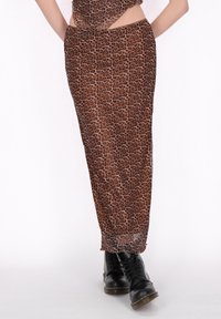 Fustă lungă cu print leopard, realizată dintr-un material transparent, având o fenduă înaltă și asortată cu bocanci negri cu șireturi pentru un contrast îndrăzneț.