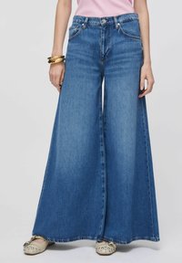 Jean en denim bleu clair à jambes larges, doté d'une taille haute, d'un design à cinq poches et d'un ourlet effiloché. Associé à des ballerines beige ornées de détails.