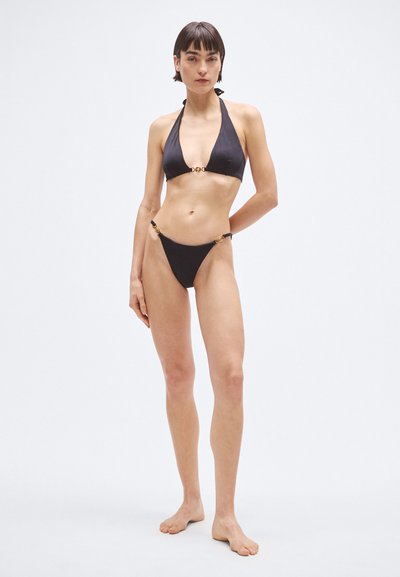 Fekete bikini szett, amely háromszög alakú felsőből áll, nyakpántos megkötőkkel, arany díszítésekkel, valamint oldalán fémes részletekkel ellátott, hozzáillő alsóval.