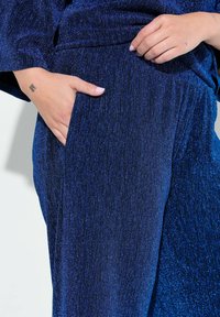 Tessuto blu profondo e testurizzato con una sottile lucentezza, con una tasca laterale visibile. Design morbido e fluido con una vestibilità ampia e rilassata.