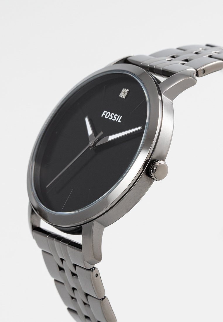 Reloj de acero inoxidable plateado con una esfera negra, diseño minimalista, manecillas delgadas y una pulsera de eslabones texturizados. Presenta la marca FOSSIL.
