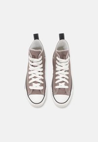 High-top sneakers in light brown canvas, featuring white laces, rubber toe cap, black heel tab, and contrasting stitching on the upper.