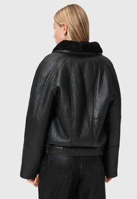 Zwarte leren jas met een gestructureerde, fuzzy kraag. Heeft een ontspannen pasvorm en opvallende stiksels op de rug. Gestyled met zwarte jeans.