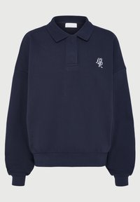 Tummansininen pitkähihaisen polo-sweater, jossa on ribbikujat ja helma, ja vasemmassa rinnassa pieni valkoinen brodeerattu logo.