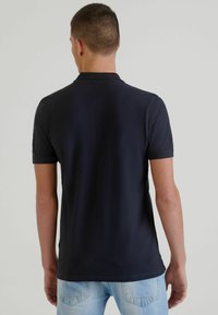 Polo shirt navy a maniche corte con colletto classico, tessuto liscio e design attillato, abbinato a jeans azzurri chiari.