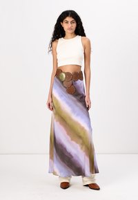 Fehér cropped top, hosszú, lebegő szoknyával, amelyet lila, zöld és barna akvarell minták díszítenek, kerek barna övvel és nagy hardverelemekkel kiemelve.