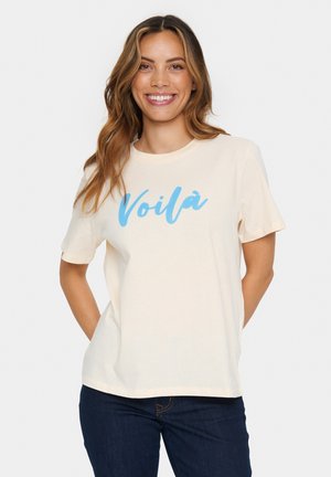 T-shirt crème à manches courtes avec le texte "Voilà" en bleu dans une police cursive. Le tissu semble doux et léger, idéal pour une tenue décontractée.