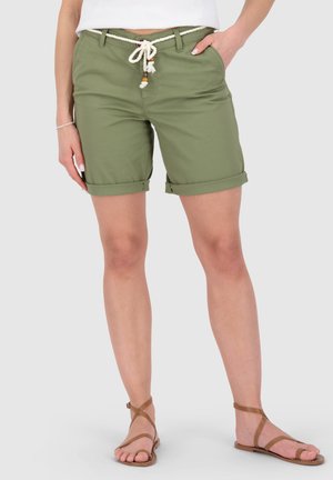 Mittellange olivgrüne Shorts mit umgeschlagenen Säumen, weißem Seilgürtel, kombiniert mit weißem Oberteil und hellbraunen flachen Riemchensandalen.