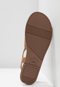 Semelle de sandale marron avec une bande de roulement texturée, logo TOMS et marquage de taille W6 1/2 visibles sur fond blanc uni.