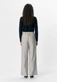 Gestreifte weit geschnittene Hosen mit einem elastischen Bund, die ein helles Farbschema aufweisen und über zwei Gesäßtaschen verfügen. Kombiniert mit einem schwarzen Pullover.