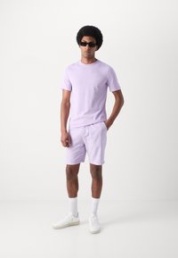 Lilla t-skjorte og shorts i bomull, med rund hals og avslappet passform. Hvite sneakers og ankelsokker fullfører antrekket.