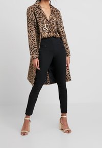 Długa kurtka w panterkę, bluzka w panterkę, czarne dopasowane spodnie oraz beżowe sandały na słupku. Gładki materiał i dopasowany krój.
