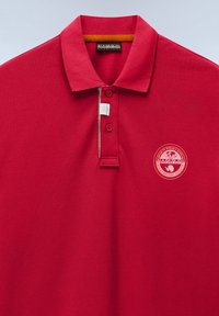 Polo rouge avec col, deux boutons et un patch logo rond Napapijri sur le côté gauche de la poitrine.