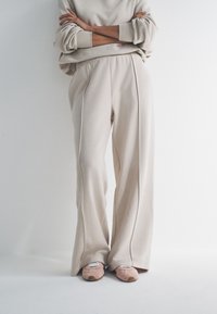 Beežist dressipluus laiade varrukatega ja sobivate laia lõikega dressipükstega, pehme tekstuuri ja mugava sobivusega. Kandmisel heleroosad kingad.