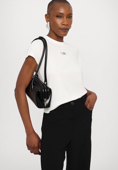 White t-shirt with a small logo, paired with high-waisted black pants and a black leather handbag featuring a curved design.