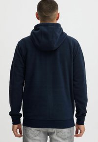 Sudadera de forro polar azul marino con capucha ajustable, puños y dobladillo acanalados. Vista trasera que muestra una textura suave y sin logotipos ni adornos visibles.