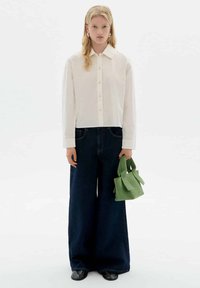 White button-up shirt, dark wide-leg jeans, black shoes, holding a green textured handbag with tied straps. Simple and minimalistic outfit.