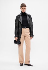 Μαύρη δερμάτινη τζακέτα μοτοσικλετιστή, μαύρο ζιβάγκο, ανοιχτό ροζ παντελόνι με κεντήματα, μαύρη τσάντα και παπούτσια με μυτερή μύτη και μεταλλικές καρφίτσες.