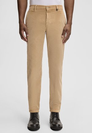 Beige corduroy broek met een smalle pasvorm, voorzien van een knoopsluiting en twee voorzakken, gecombineerd met zwarte enkellaarsjes met veters.