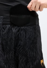 Μαύρα αθλητικά σορτς με διακριτικό υφασμάτινο σχέδιο, που διαθέτουν τσέπη με βέλκρο στη μέση και χρυσό λογότυπο ως λεπτομέρεια στο πλάι.