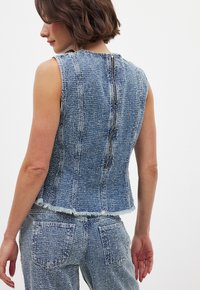 Denim gilet in lichtblauw met een gestructureerde oppervlakte, mouwloos ontwerp, raw hem, en een rits sluiting aan de achterkant.