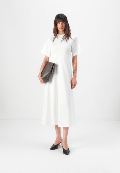 Weißes Midi-Kleid mit kurzen Ärmeln, rundem Ausschnitt und fließender Silhouette. Dazu eine dunkelbraune Clutch und schwarze slingback Absatzschuhe.