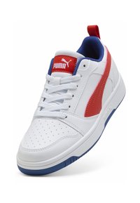 Baskets blanches avec des accents rouges et bleus, présentant une tige en cuir texturé, un système de laçage, un bout perforé et une semelle en caoutchouc bleu.