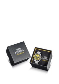 Sudraba metāla pulkstenis ar dzeltenu ciparnīcu, izstādīts melnā tekstūrētā kastē ar Festina logo un zelta burtiem.