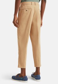 Pantalones beige con corte recto, que cuentan con bolsillos traseros y costuras sutiles. Se destaca la textura de la tela y la longitud recortada por encima del tobillo.