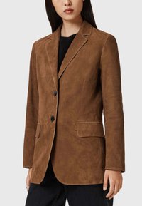 Bruine suède blazer met een notch-revers, enkele knoopsluiting en twee voorkruiden. Kenmerkt zich door een gladde textuur en een getailleerde pasvorm.