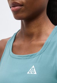 Κοντινό πλάνο μιας γυναίκας που φοράει ανοιχτό μπλε αθλητικό τοπ με λευκό λογότυπο ACG στο στήθος.