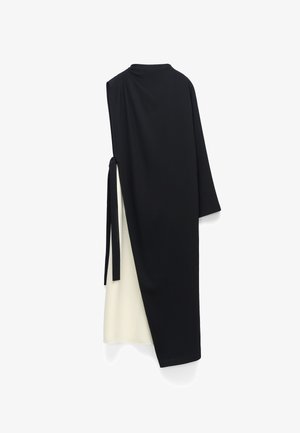 Asymetryczna czarno-biała sukienka midi z jednym długim rękawem i ozdobą zawiązaną z boku na białym tle.