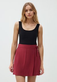 Zwarte geribbelde tanktop gecombineerd met een bordeauxrode wikkelrok. De rok heeft een strik aan de zijkant en plooien voor extra detail.