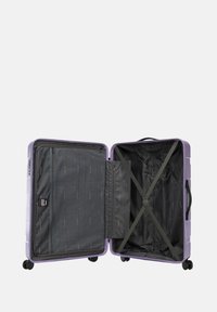 Valigia rigida di colore viola chiaro con interni neri, dotata di una tasca con zip, cinghie a X per fissare il contenuto e quattro ruote.